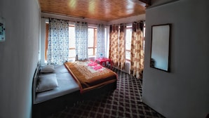 A bedroom with a wooden ceiling, a bed with a patterned bedspread, a red chair, and a window with patterned curtains. - Royal palace  (Anantnag)