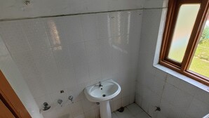A small, basic bathroom with a toilet, sink, and window. - Royal palace  (Anantnag)