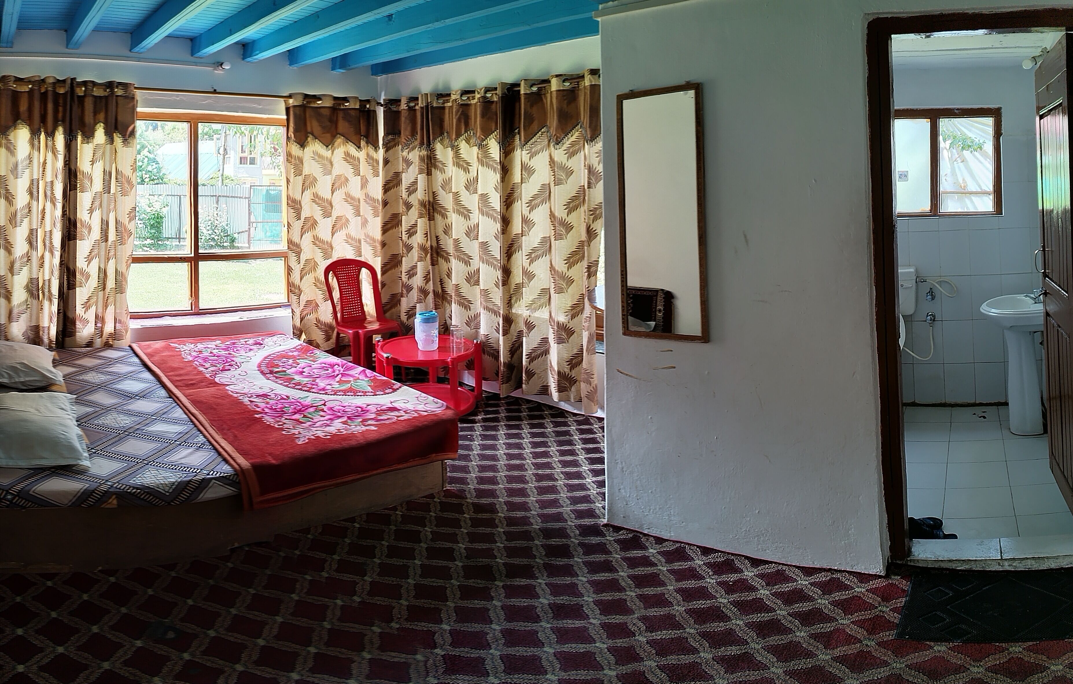 A bedroom with a bed, a red chair, a large window, and a bathroom visible through an open door.