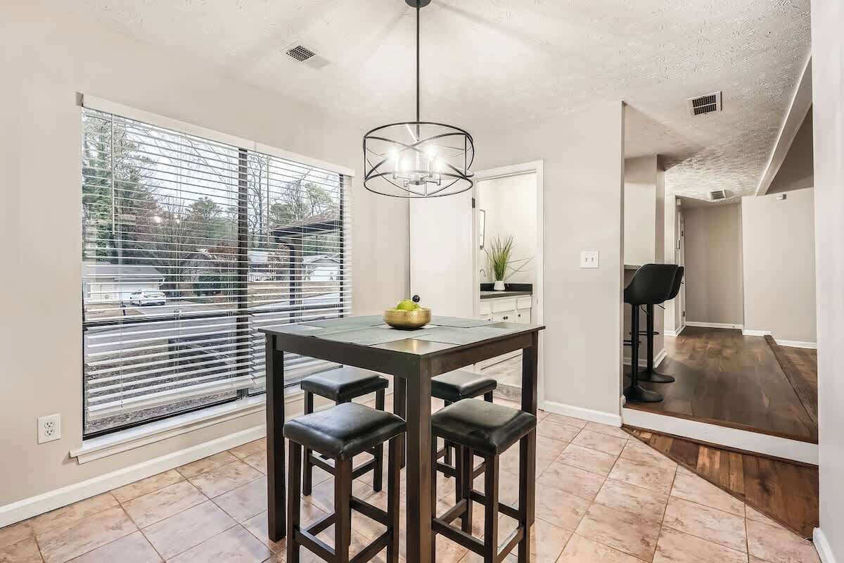 A modern kitchen with a dining table, bar stools, and a pendant light.