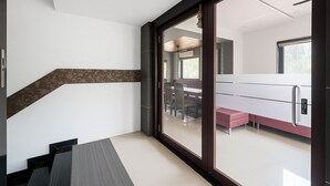 A modern interior with a staircase, a dining area with a table and chairs, and a kitchen with a refrigerator. - The Grantley Hotel (Alibag)