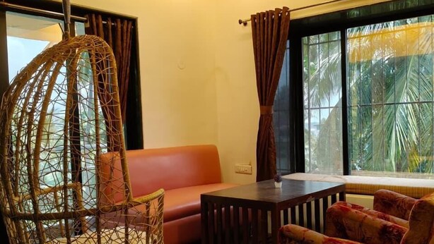 A room with a hanging chair, a sofa, a table, and a ceiling fan. - The Grantley Hotel (Alibag)