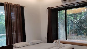 A bedroom with a bed, a chair, a window with curtains, an air conditioning unit, and a ceiling fan. - The Grantley Hotel (Alibag)