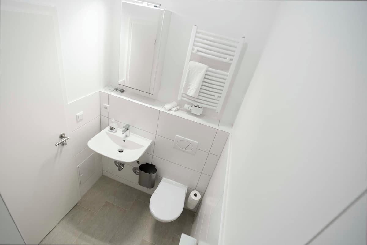A small, white bathroom with a sink, mirror, towel rack, and toilet.