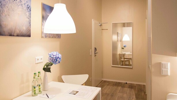 A hotel room with a white table, chairs, a white vase with a blue flower, and two bottles of water. - GuestHouse Köhn51 (Nuremberg)