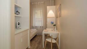 A small, well-lit room with a bed, a table with a chair, a coffee maker, and a lamp. - GuestHouse Köhn51 (Nuremberg)
