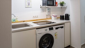 A compact kitchen with a washing machine, microwave, and a small shelf with a plant. - GuestHouse Köhn51 (Nuremberg)
