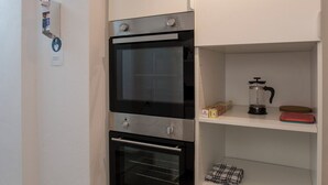 A kitchen with two ovens, a coffee maker, and a red cutting board on a shelf. - GuestHouse Köhn51 (Nuremberg)