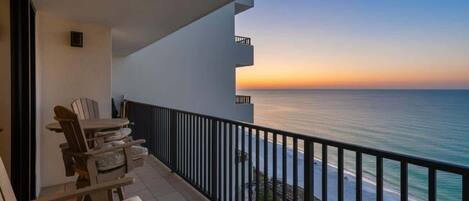 A balcony with a view of the ocean at sunset, outdoor seating, and a sign indicating the room number.