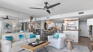 A modern living room with a white sofa, coffee table, and a dining area with a round table. - Seagrove Beachfront Condo with Incredible Views (Santa Rosa Beach)