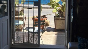 Puerta abierta que da a un balcón con vista al mar, una planta de cactus y mobiliario de exterior.