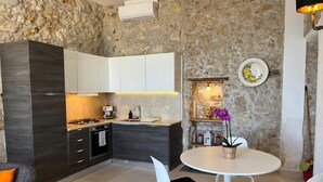 Una cocina moderna con un fondo de pared de piedra, una zona de comedor con sillas blancas y una pequeña mesa.