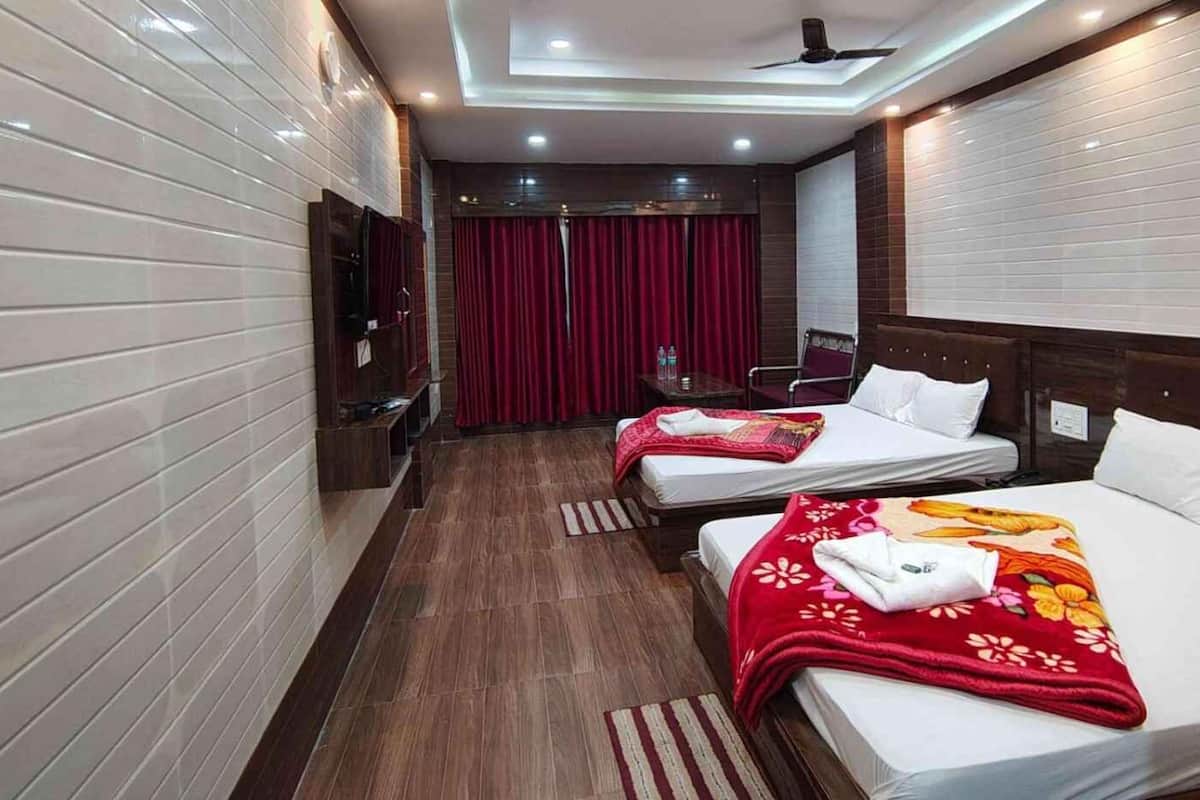 A hotel room with two beds, a TV, a ceiling fan, and a red curtain.