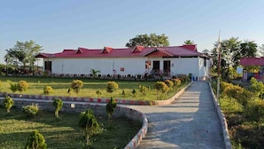 A pathway leading to a building with a red roof, surrounded by greenery and a clear sky. - Amantran Hotel & Resort (Alipurduar)