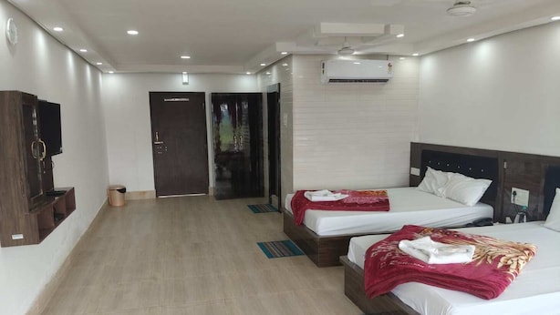 A hotel room with two beds, a TV, an air conditioning unit, and a small trash bin. - Amantran Hotel & Resort (Alipurduar)