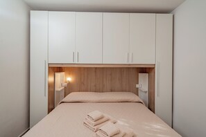 A bedroom with a bed, a wooden headboard, and a wall-mounted light fixture. - Casa Donatella (Orosei)