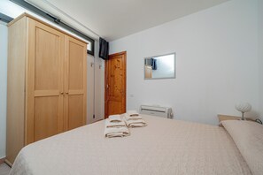 A bedroom with a large wardrobe, a bed with neatly folded towels, a radiator, and a mirror on the wall. - Casa Donatella (Orosei)