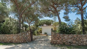 A stone gate leading to a building with a tiled roof, surrounded by trees and a stone wall. - Casa Donatella (Orosei)