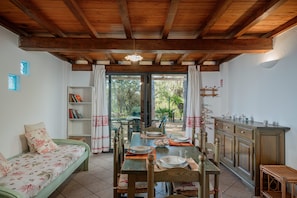 A cozy room with a wooden ceiling, a dining table set for two, a sofa, and a bookshelf. - Casa Donatella (Orosei)