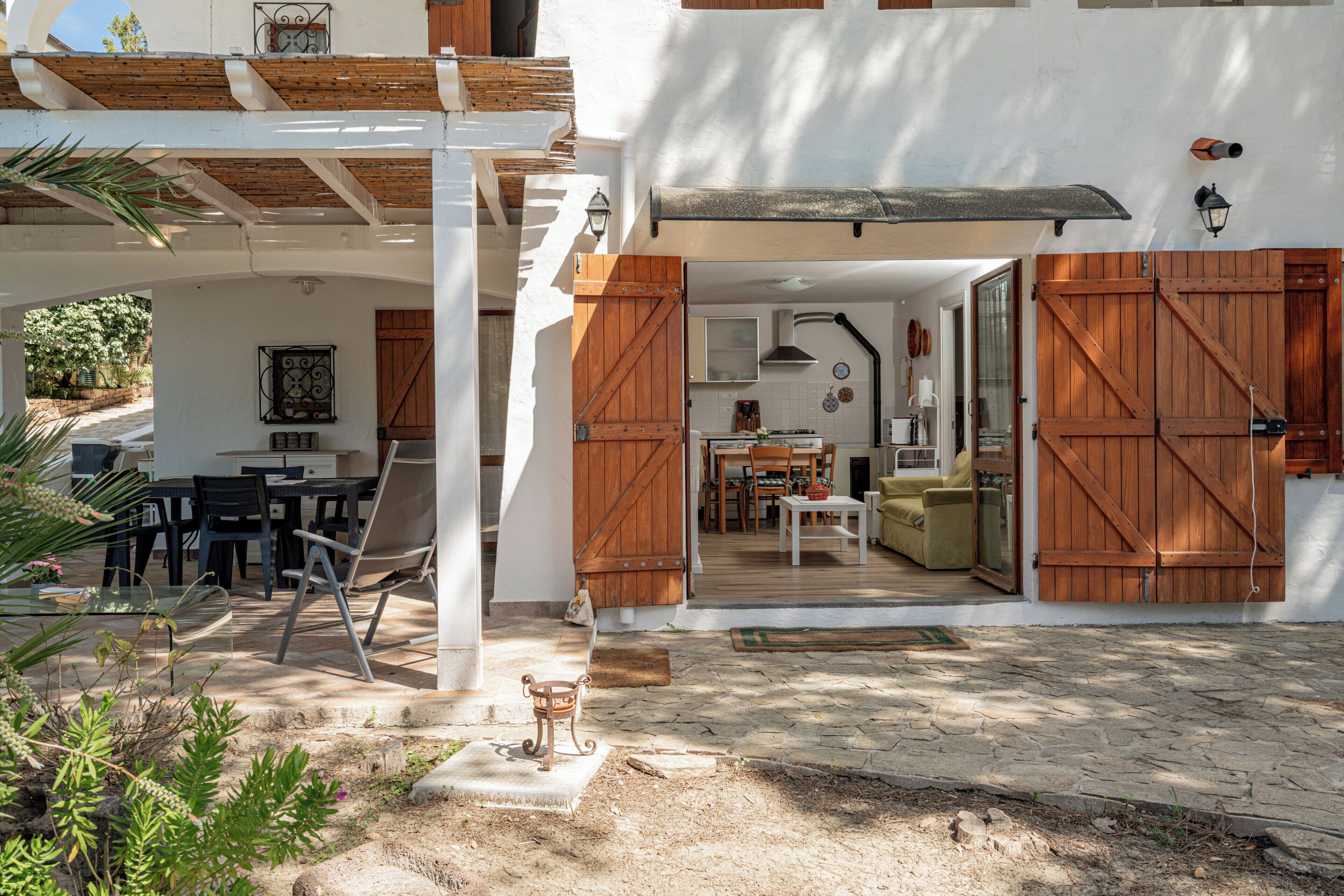 A covered outdoor area with a dining table and chairs, a wooden bench, and a rustic door.