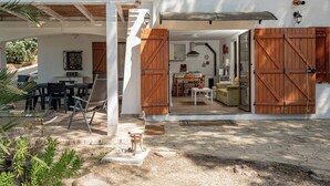 A covered outdoor area with a dining table and chairs, a wooden bench, and a rustic door. - Casa Donatella (Orosei)