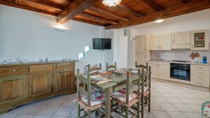 A spacious kitchen with wooden cabinets, a dining table set for four, and a built-in oven. - Casa Donatella (Orosei)
