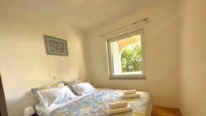 A bedroom with a bed, a window, a nightstand, and a framed picture on the wall. - Apartman Portos (Crikvenica)