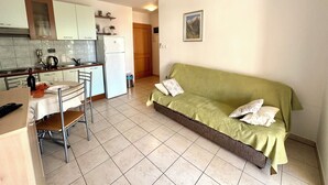 A compact living space with a kitchenette, a dining area, and a green sofa. - Apartman Portos (Crikvenica)