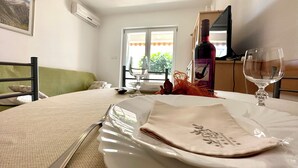 A dining area with a table set for two, a wine bottle, and a glass on the table. - Apartman Portos (Crikvenica)