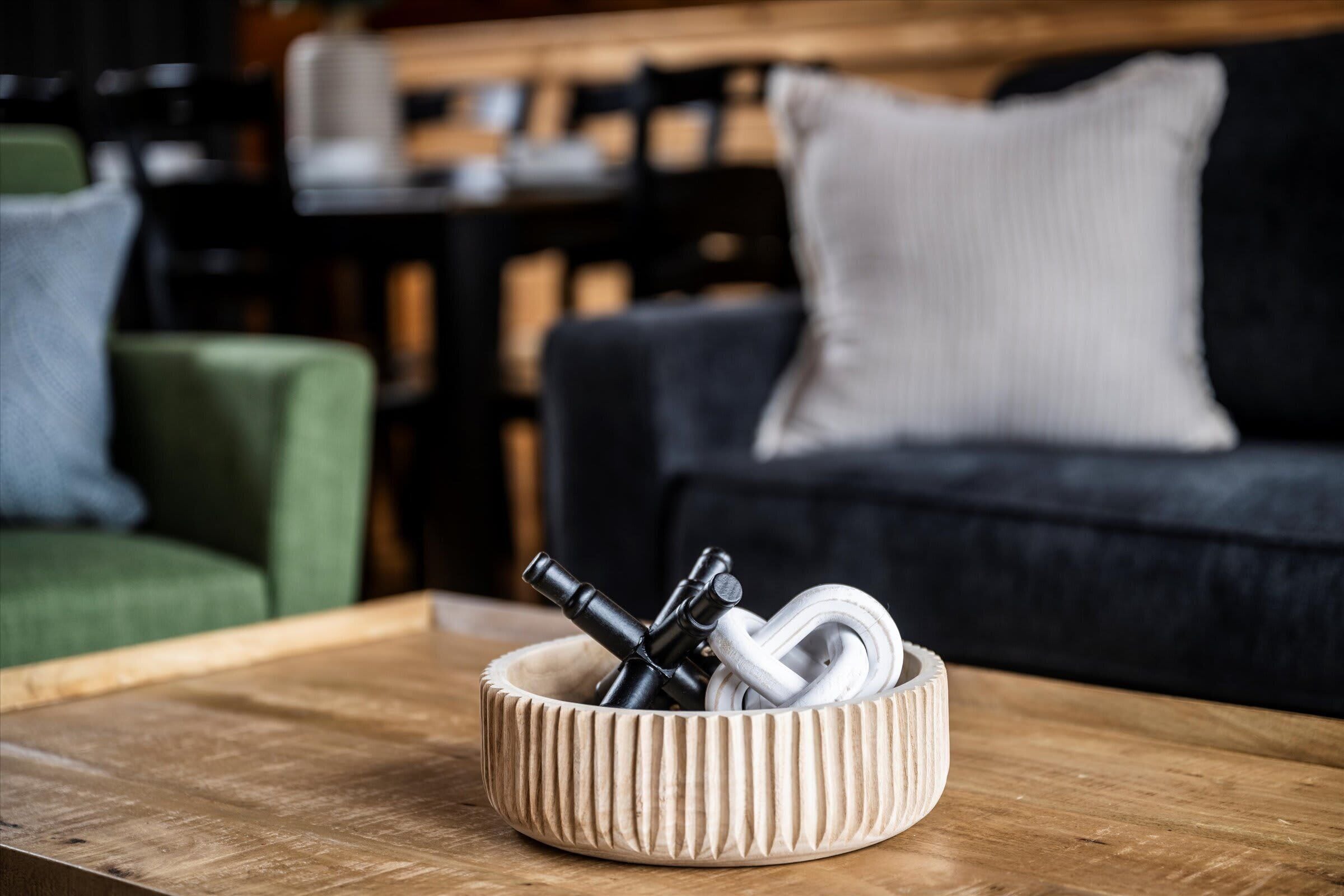 A wooden table with a ribbed bowl containing a metal object and a white cable.