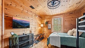 Una habitación tipo cabaña acogedora con detalles de madera, una cama, un escritorio, un televisor y una ventana con vistas.