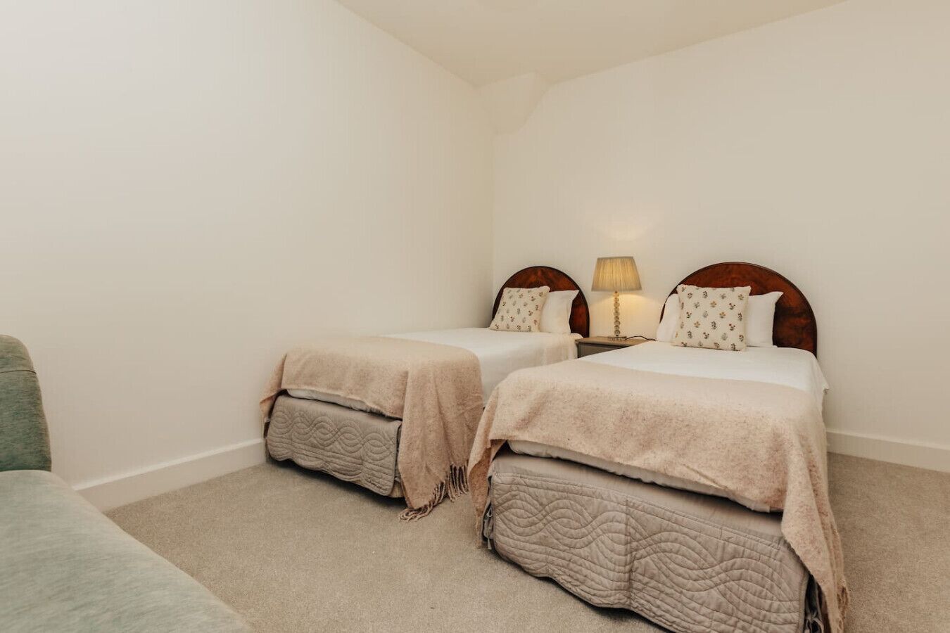 Une chambre avec deux lits simples, chacun doté d’une tête de lit en bois, d’une table de chevet et d’une lampe. Les murs de la chambre sont d’un blanc uni et le sol est recouvert d’une moquette.