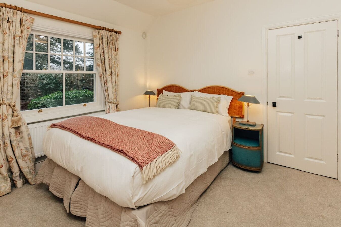 Een slaapkamer met een groot bed, twee nachtkastjes, een raam met gordijnen en een deur.