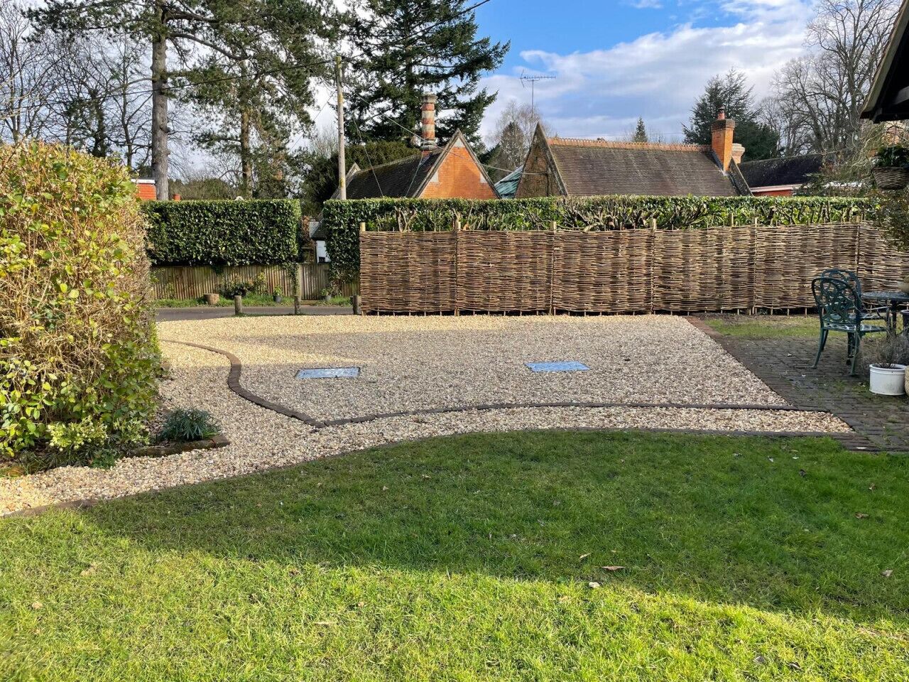 Un jardin avec un espace recouvert de gravier, une pelouse et une clôture en bois.