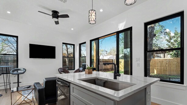 A modern kitchen with a large island, black bar stools, and a ceiling fan.