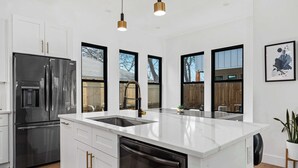 A modern kitchen with white cabinetry, stainless steel appliances, a large island with a sink, and pendant lighting.