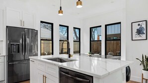 A modern kitchen with white cabinetry, stainless steel appliances, a large island with a sink, and pendant lighting. - Downtown ATX - Unit A | Modern Home | Pool (Austin)