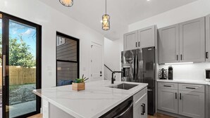 A modern kitchen with a large island, stainless steel appliances, and light grey cabinetry.