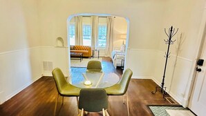 Un coin repas avec une table ronde, quatre chaises, un ventilateur de plafond et une vue sur une chambre à coucher, visible à travers un miroir.