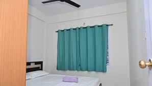 Un dormitorio con cama, ventilador de techo y ventana con cortinas color turquesa.