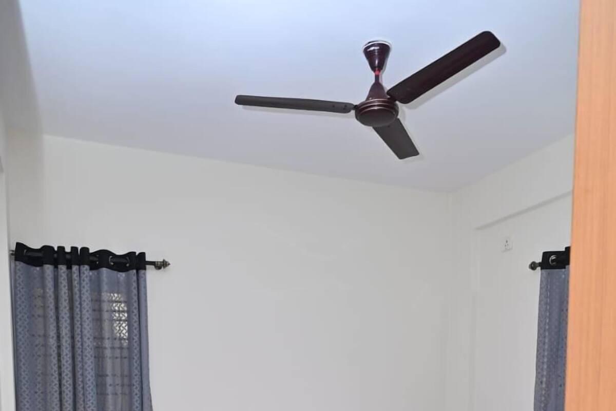 A neatly made bed with a wooden headboard, a ceiling fan, and a patterned rug on the floor.