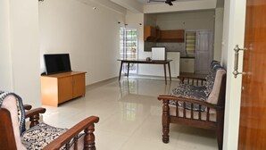 Amplia sala de estar con televisor, muebles de madera, una mesa de comedor y una cocina al fondo.