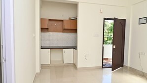 Una cocina con armarios de madera y un salpicadero de azulejos, una puerta que da al exterior, y un suelo limpio con baldosas.