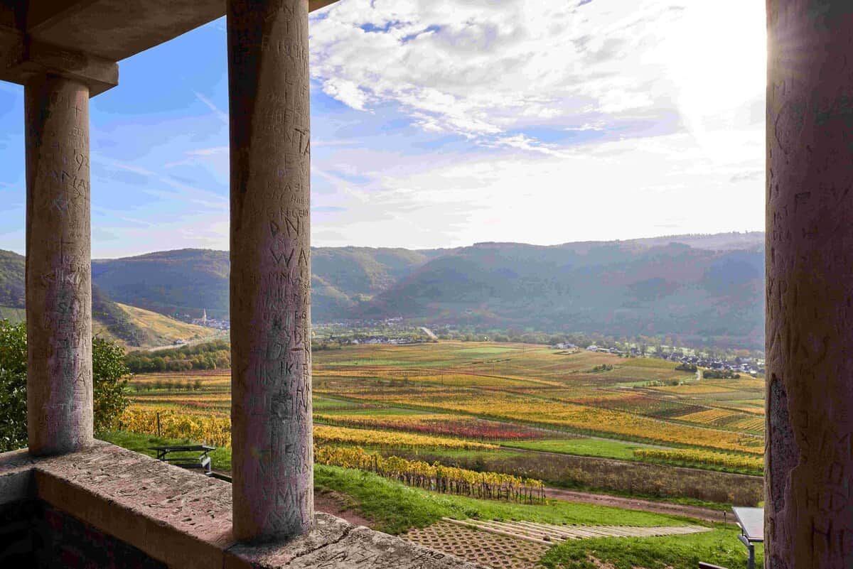 Une vue depuis un espace abrité, doté de colonnes, qui donne sur une vallée avec des champs agricoles et des collines lointaines.