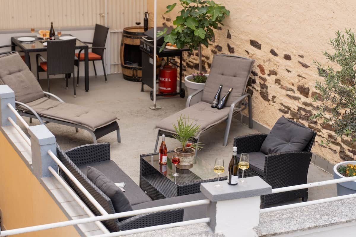 An outdoor patio area with wicker furniture, a table with wine bottles, and a barrel.