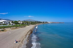 Una playa con vista despejada del océano, orilla arenosa y edificios al fondo.