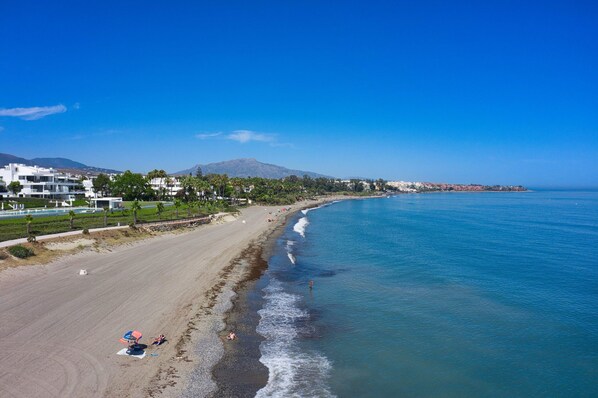 Una playa con vista despejada del océano, orilla arenosa y edificios al fondo.