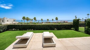 A terrace with two sun loungers, a well-maintained lawn, and a view of the sea and palm trees. - 3001 Velaya Beachfront Luxury Apartment (Estepona)