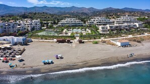 A coastal resort with multiple white buildings, a sandy beach, and a clear blue sky. - 3001 Velaya Beachfront Luxury Apartment (Estepona)