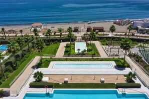 Un resort con una gran piscina, palmeras y vista a la playa.